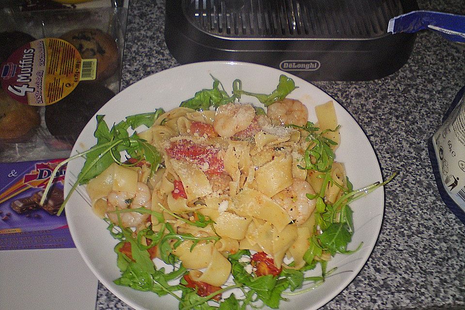 Bandnudeln Aglio e Olio mit Cocktailtomaten und Shrimps auf einem Bett aus Rucola