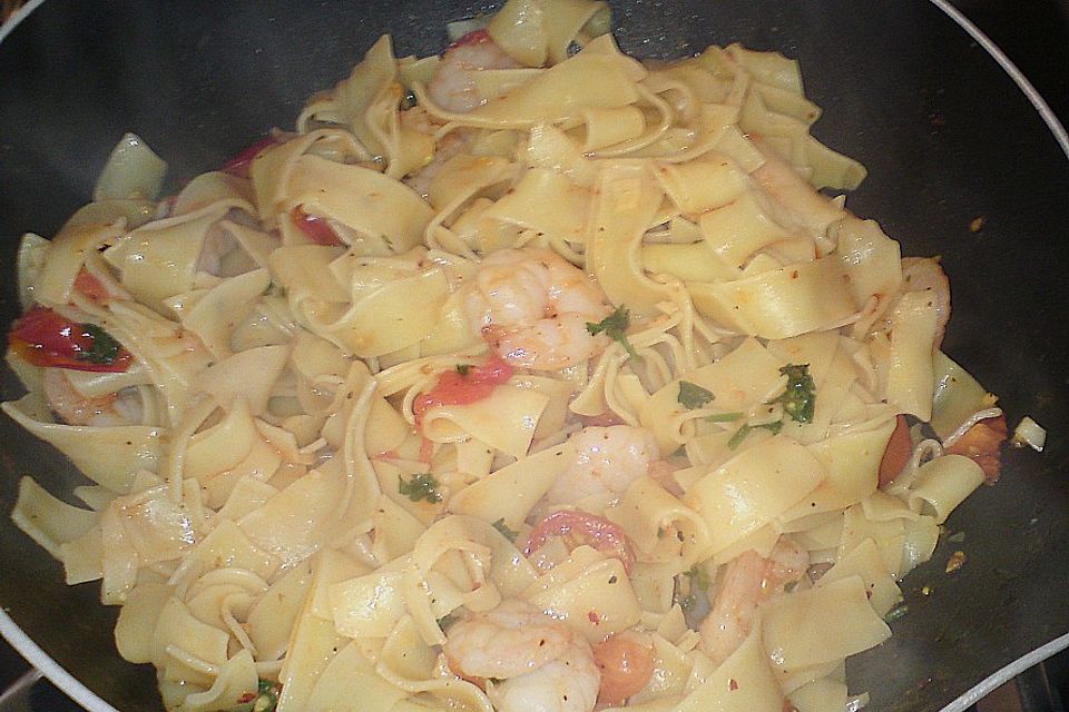 Bandnudeln Aglio e Olio mit Cocktailtomaten und Shrimps auf einem Bett aus Rucola