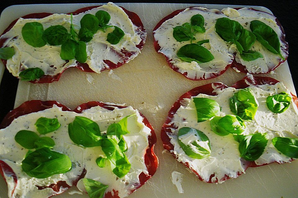 Parmaschinkenröllchen mit Frischkäse und Basilikum auf Röstbrotscheiben