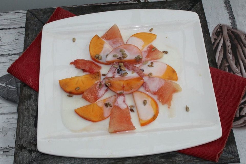 Melonen-Kaki-Nachspeisenteller mit Buttermilch-Honig-Sauce und gerösteten Sonnenblumenkernen