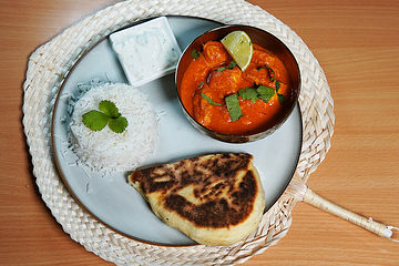 Buttriger Gockel an weißem Korn, indischer Knifte und Gurken-Minz-Raita - indisches Butter-Chicken mit Reis, Naan-Brot und Gurken-Minz-Raita