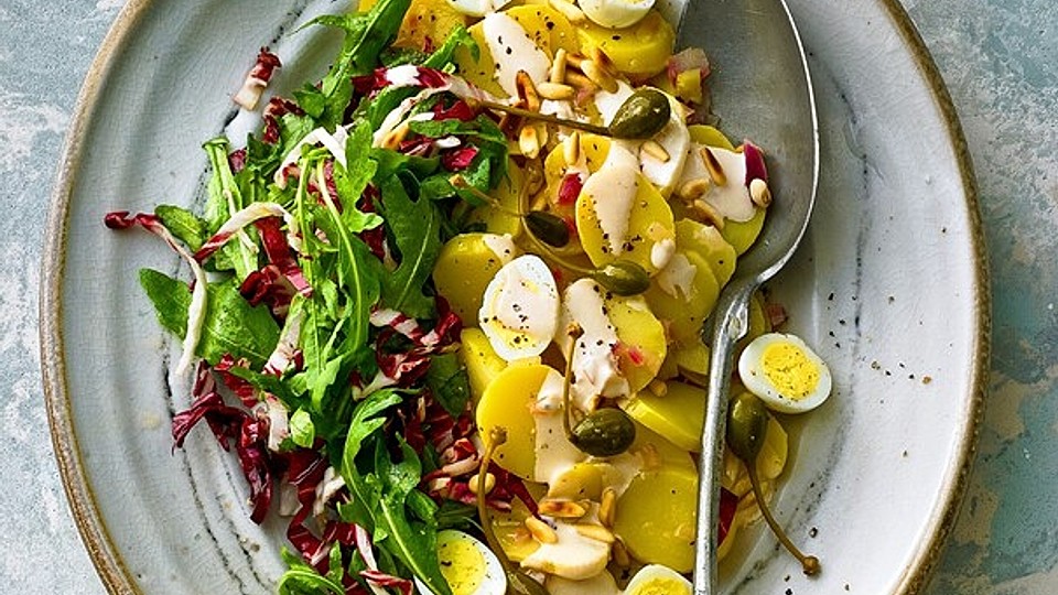 Andalusischer Kartoffelsalat mit Thunfisch, garniert mit Pinienkernen, Kapern und frischen Radicchio-Streifen auf rustikalem Holzbrett