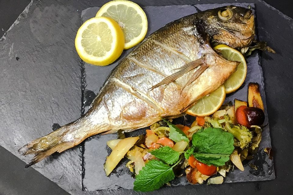 Ganzer Fisch auf Kartoffeln und Gemüse